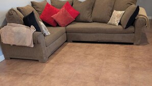 Un divano angolare marrone con numerosi cuscini, una coperta e un pavimento piastrellato.