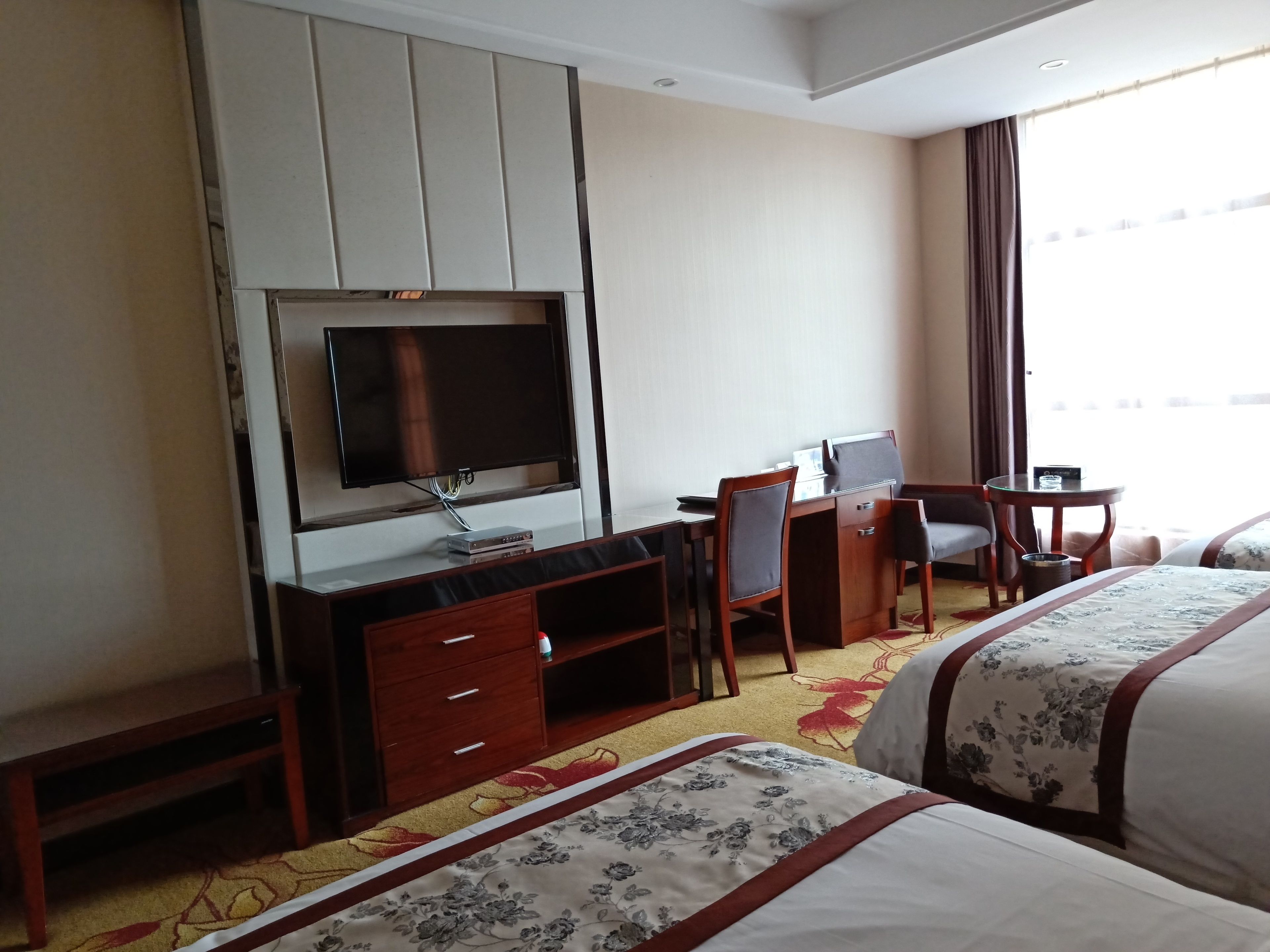Una habitació d'hotel amb un llit, escriptori amb cadira, televisió i una taula petita.