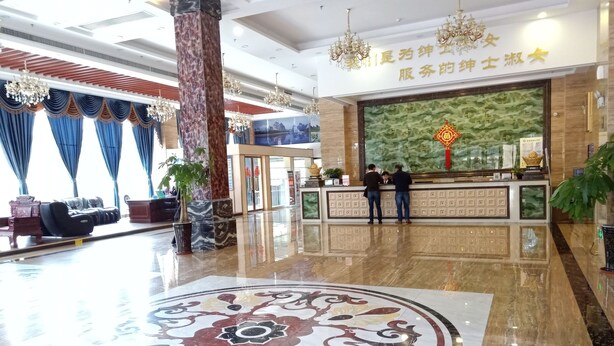 Un hall d’hôtel avec un comptoir d’accueil, deux hommes debout derrière le comptoir et un grand motif décoratif sur le sol.