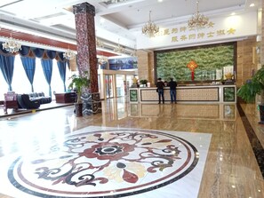 A hotel lobby with a reception desk, two men standing at the counter, and a large decorative floor pattern. - Guilin Xin Bin International Hotel (Guilin)