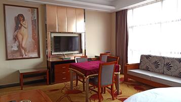 A hotel room with a bed, a desk with a TV, a dining table, and a sofa.