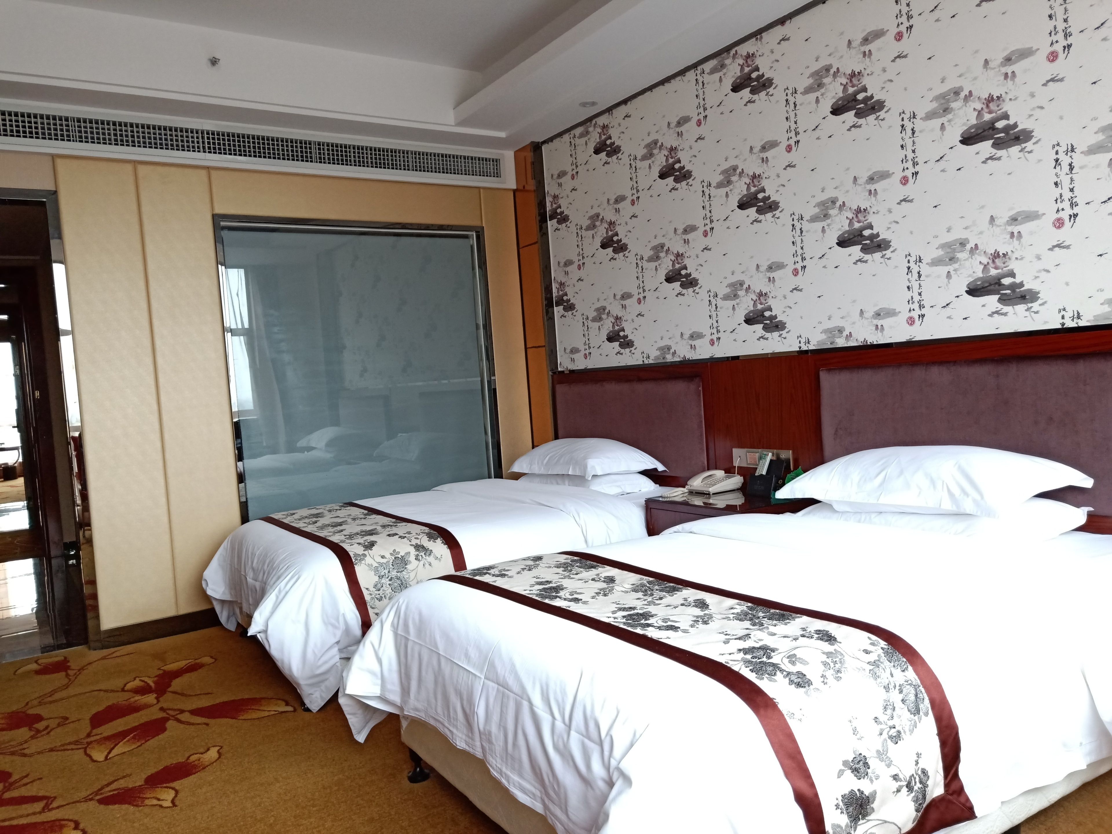 Een hotelkamer met twee bedden, een groot raam en bloemenbehang.