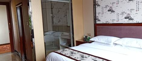 Une chambre d’hôtel avec un grand lit, une armoire, une salle de bain avec une porte en verre et un mur orné d’œuvres d’art traditionnelles.