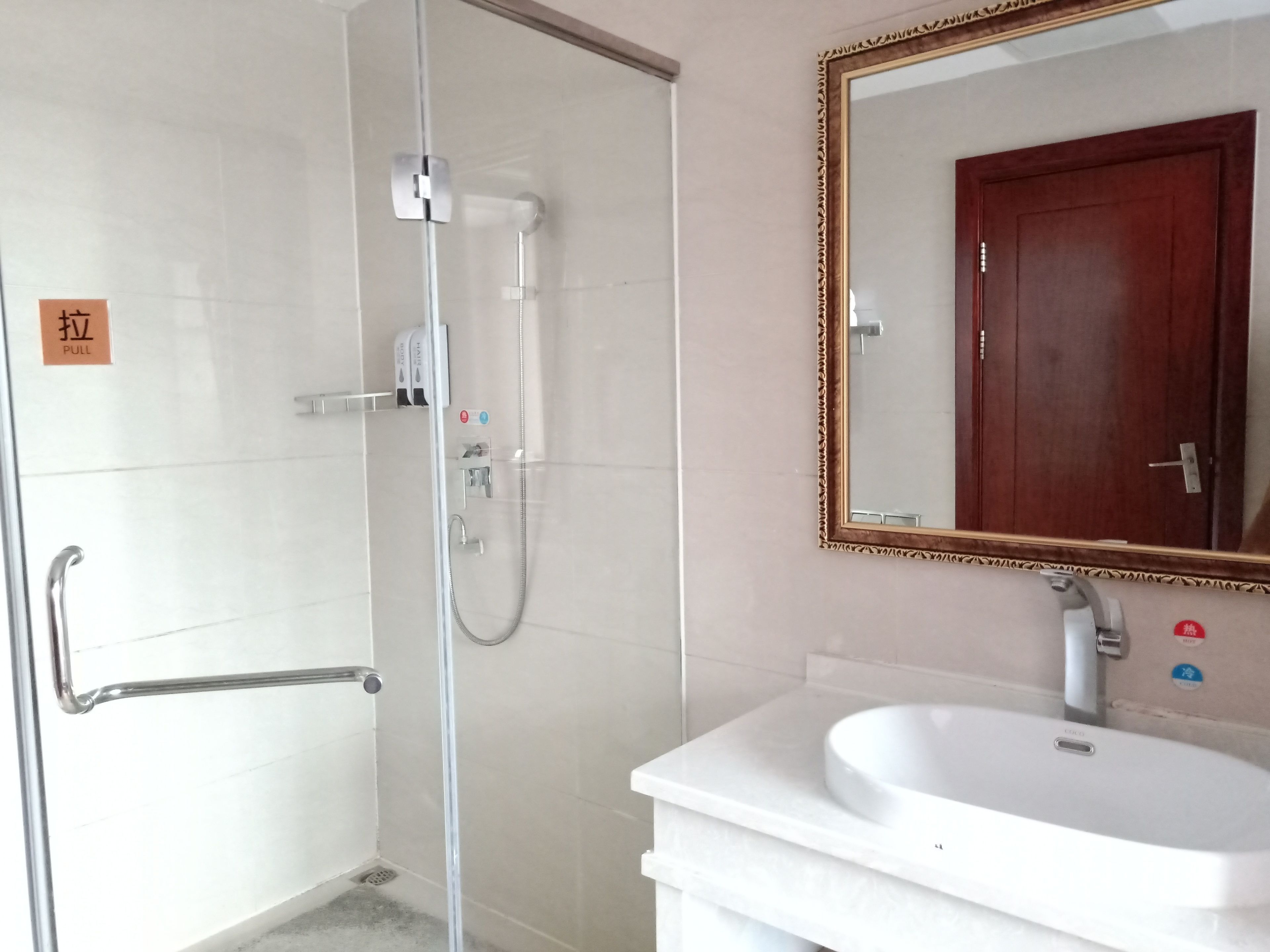 A bathroom with a glass-enclosed shower, a white sink, and a wooden door.