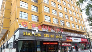 Un bâtiment jaune avec de nombreuses fenêtres et une enseigne indiquant « HÔTEL XIAO XIN BIN ».