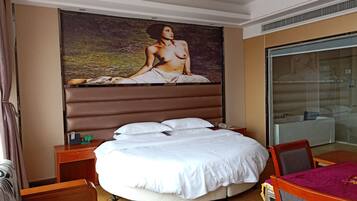 Ein Hotelzimmer mit einem großen Bett, einem Schreibtisch, einem Stuhl, einer Duschkabine aus Glas und einem Bild an der Wand.