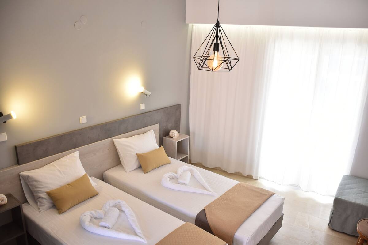 A hotel room with two beds, a nightstand, a towel rack, and a hanging light fixture.
