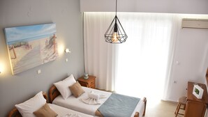 Ein Hotelzimmer mit zwei Betten, einem Meeresblick-Gemälde, einer Hängelampe und einem Schreibtisch mit Stuhl.