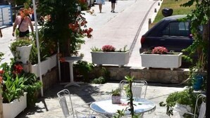 Eine Terrassengrundstück mit Steinbelag, Metallstühlen und -tischen, umgeben von Topfpflanzen und Blumen.