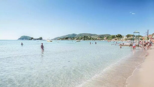 Ein Strand mit klarem Wasser, badenden Personen und einem sandigen Ufer.