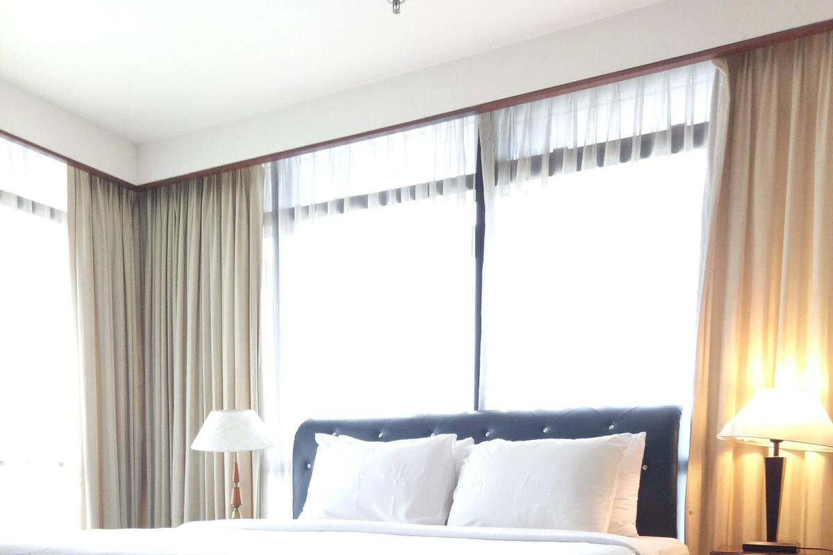 Een hotelkamer met een groot bed, een nachtkastje met een lamp en een raam met gordijnen.