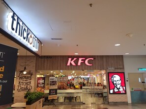 Een KFC restaurant met een opvallend bord, een groot digitaal scherm met een kok en promotiebanners.