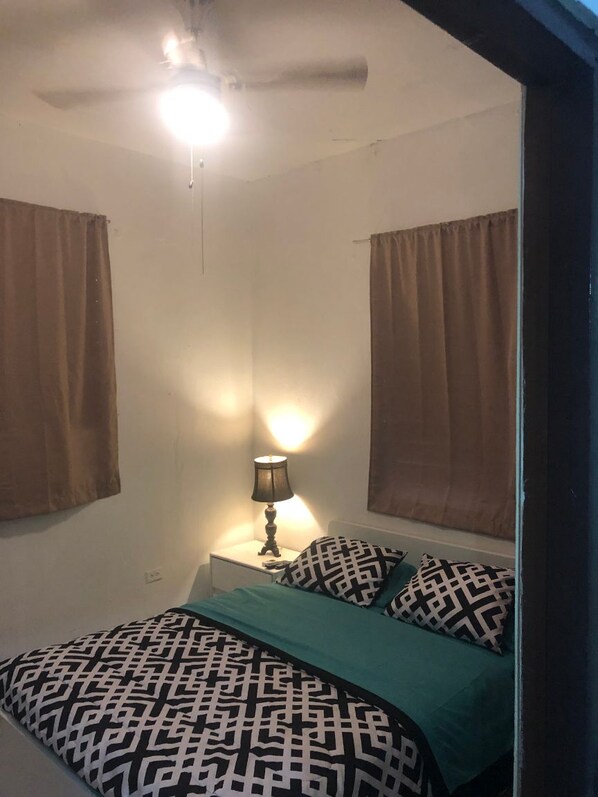 A bedroom with a bed, a nightstand with a lamp, and a ceiling fan.