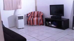 A living room with a striped armchair, a black entertainment unit with a TV, a white air conditioner, and a black sofa.