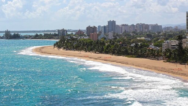 A coastal cityscape with a beach, buildings, and a clear sky.