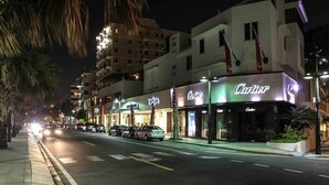 A street view at night with a row of storefronts, including a prominently lit 'Cartier' sign.