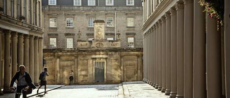 A narrow street with a building featuring classical architecture, including columns and a central entrance.