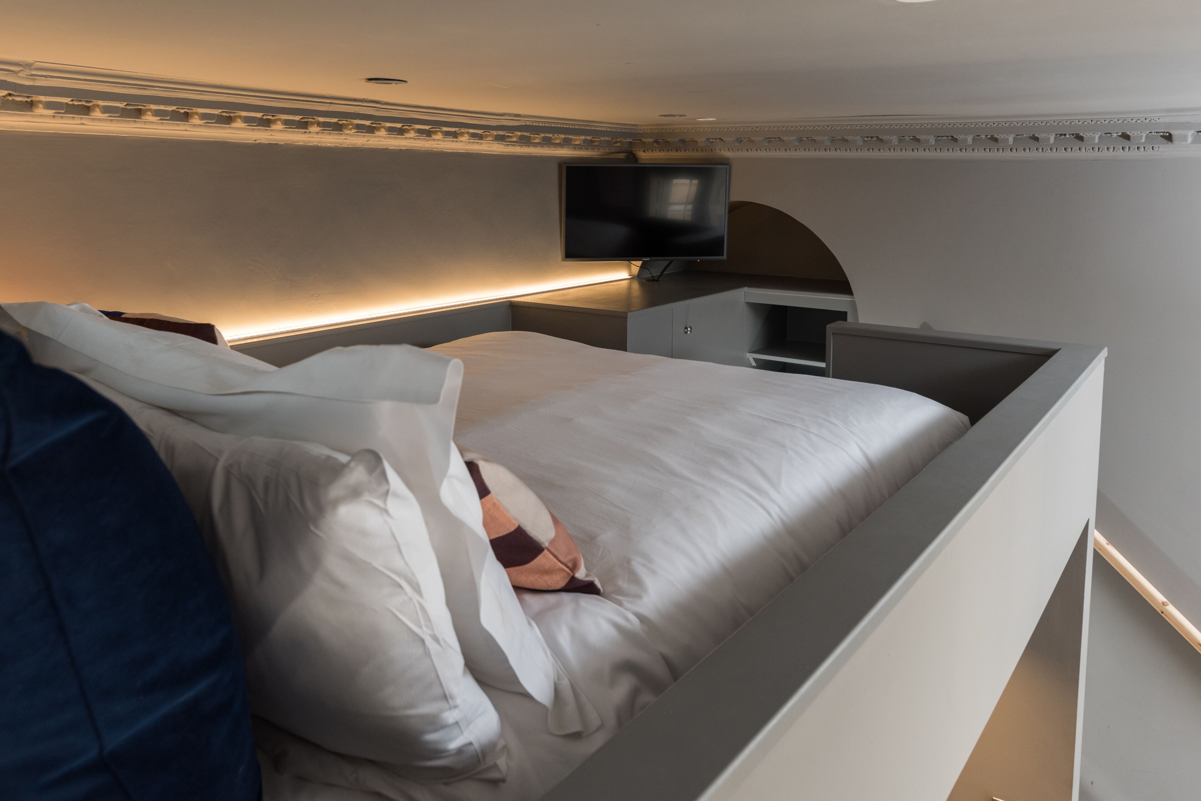 A modern bedroom with a bed, a flat-screen TV mounted on the wall, and a bedside table.