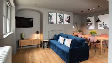 Uma sala de estar moderna com um sofá azul, piso de madeira, uma televisão e obras de arte emolduradas na parede.