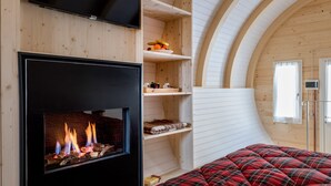 Een knus vertrek met een open haard, houten planken en een bed met een geruite deken.