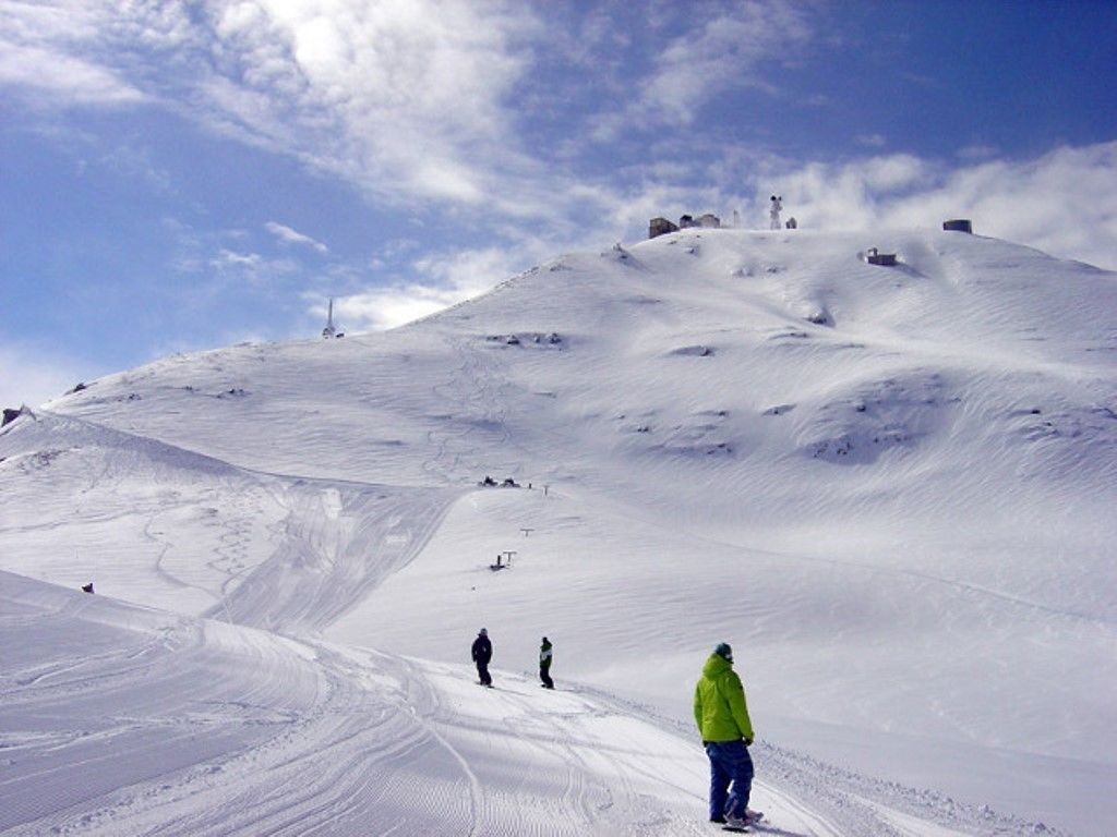 Une pente de montagne enneigée, avec des skieurs et une personne portant une veste de couleur vive.