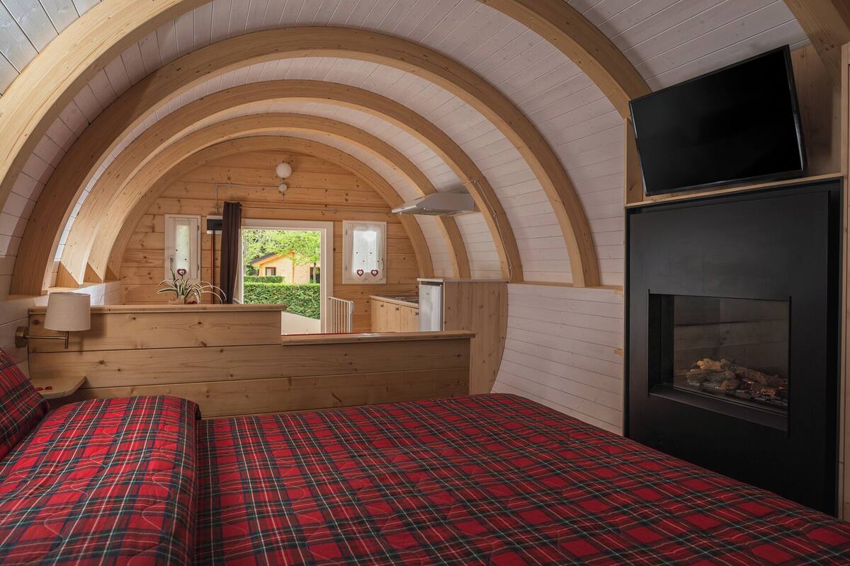 Una habitación acogedora con techo de madera, una chimenea, una cama con colcha escocesa y un televisor sobre la chimenea.