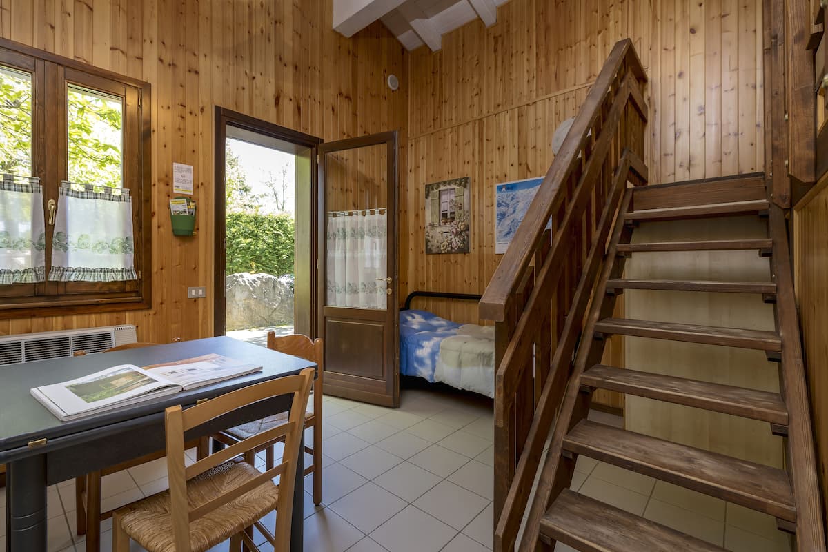 Un interior de madera con una mesa de comedor, sillas, una cama y una escalera de madera.