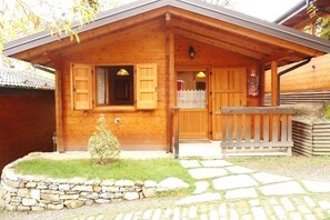 A wooden cabin with a stone foundation, a small garden, and a wooden porch. - Campeggio Parco dei Castagni srl (Montecreto)