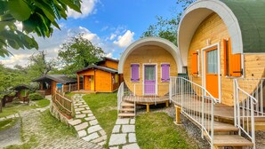 Een rij houten hutten met paarse luiken, een pad van stenen en een klein houten gebouwtje op de achtergrond.