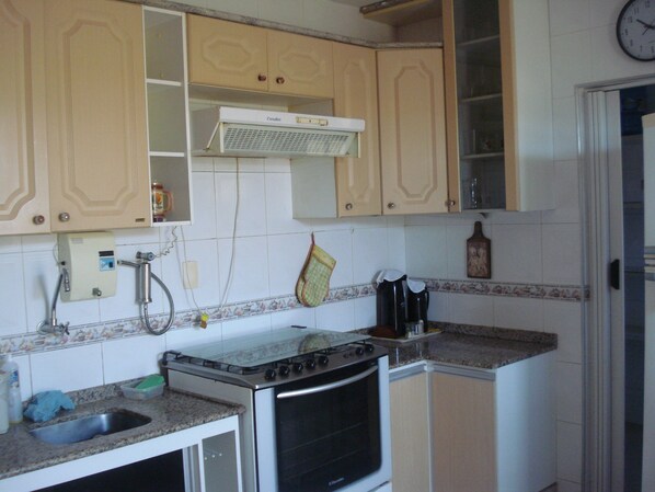 A kitchen with a stove, oven, and sink. There is a clock on the wall and a window above the sink.