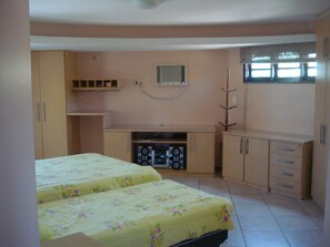 A bedroom with two beds, a small kitchenette, and a window with blinds.