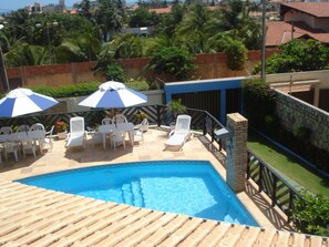 A swimming pool with lounge chairs and umbrellas, surrounded by greenery and a stone wall.