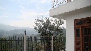 A balcony with a view of a mountainous landscape, a metal railing, and a wooden door. - Chef Guru Hotels (Bandarawela)
