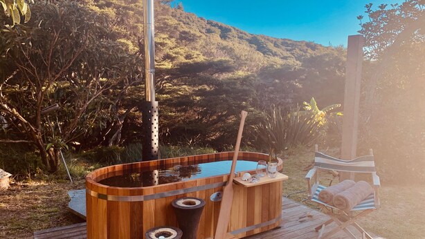 Ein hölzernes Whirlpool mit Metallstange, umgeben von einer Holzterrasse und einem Holzstuhl.