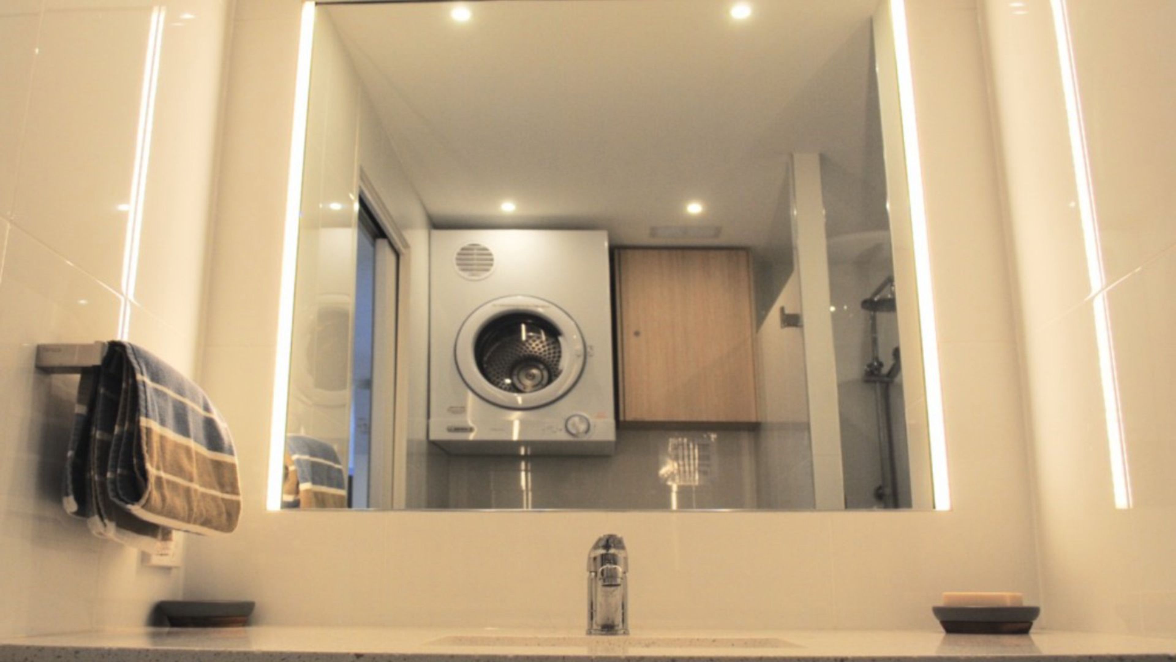 A modern bathroom with a large mirror, a sink, a shower, and a visible dryer.