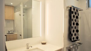 A modern bathroom with a large mirror, a sink, a towel rack with a polka-dotted towel, and a shower area. - Joanne Terrace 203 Oceanview Near Kings Beach (Caloundra)