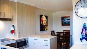 A modern kitchen with white cabinets, a microwave, and a dining area with wooden chairs.