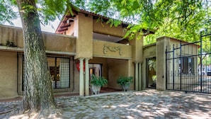 A building with a tiled roof, a gated entrance, and a paved courtyard with potted plants. - Christie's at 32 on Russell (Mbombela)