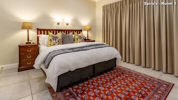 A bedroom with a bed, nightstands, lamps, a patterned rug, and a curtain.