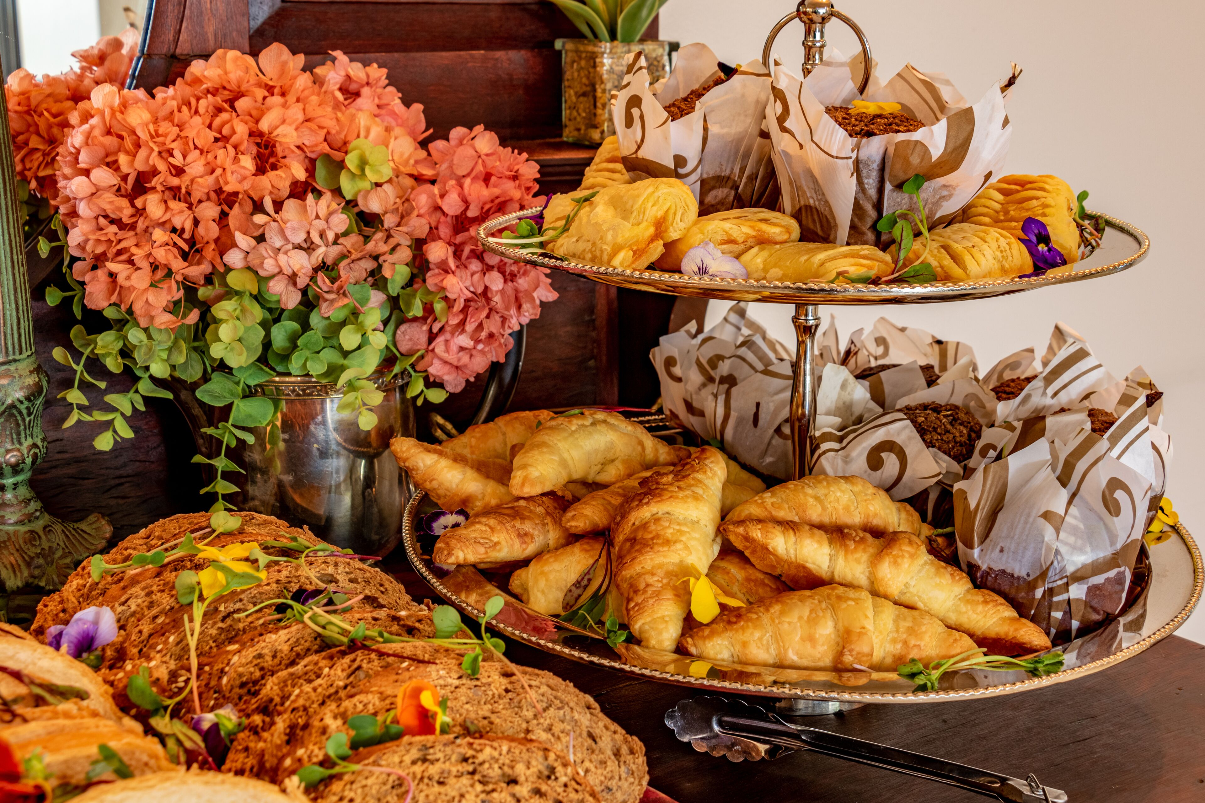 A buffet with various breads, pastries, and flowers.