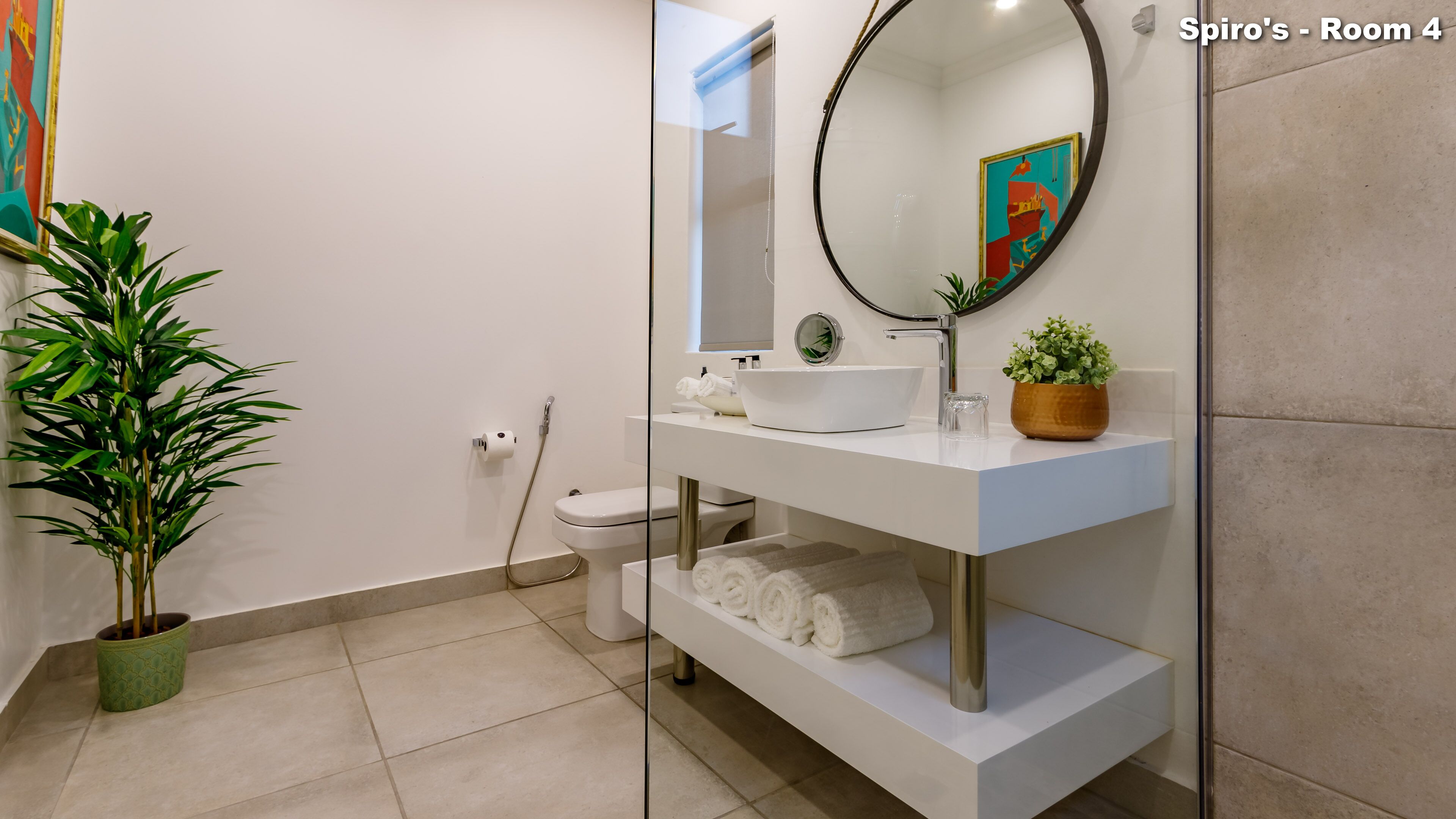 A modern bathroom with a white sink, a mirror, a toilet, and a potted plant.