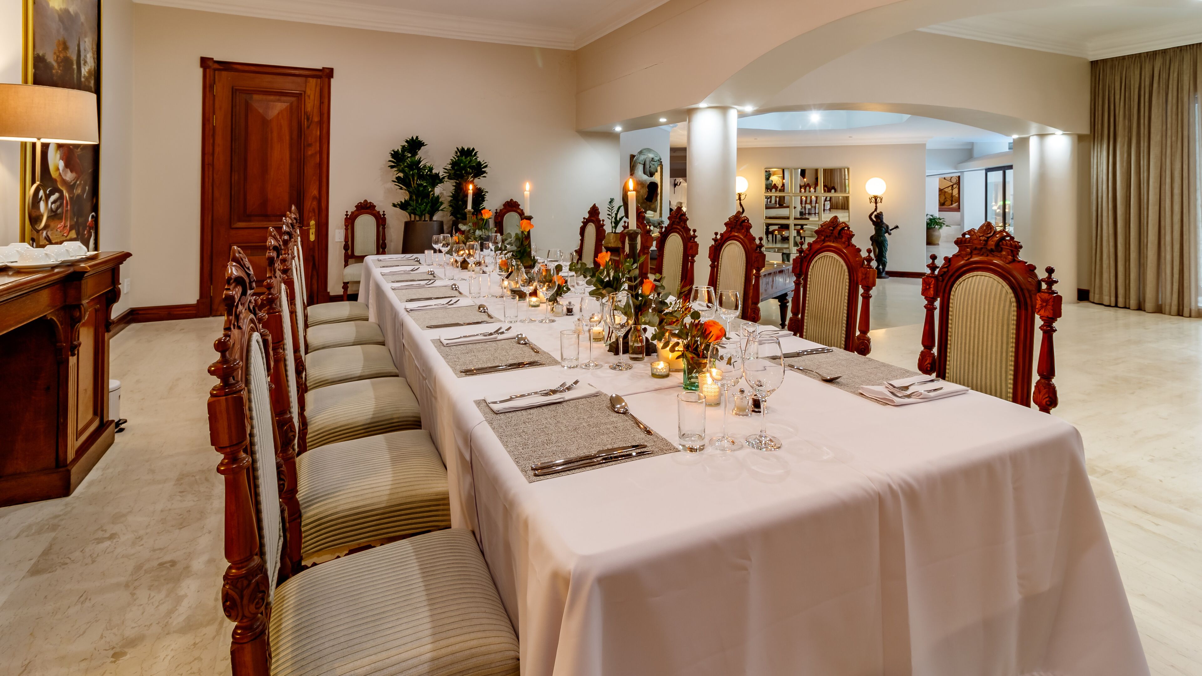 Una larga mesa de comedor preparada para una comida formal, con sillas, velas y centros de mesa florales.