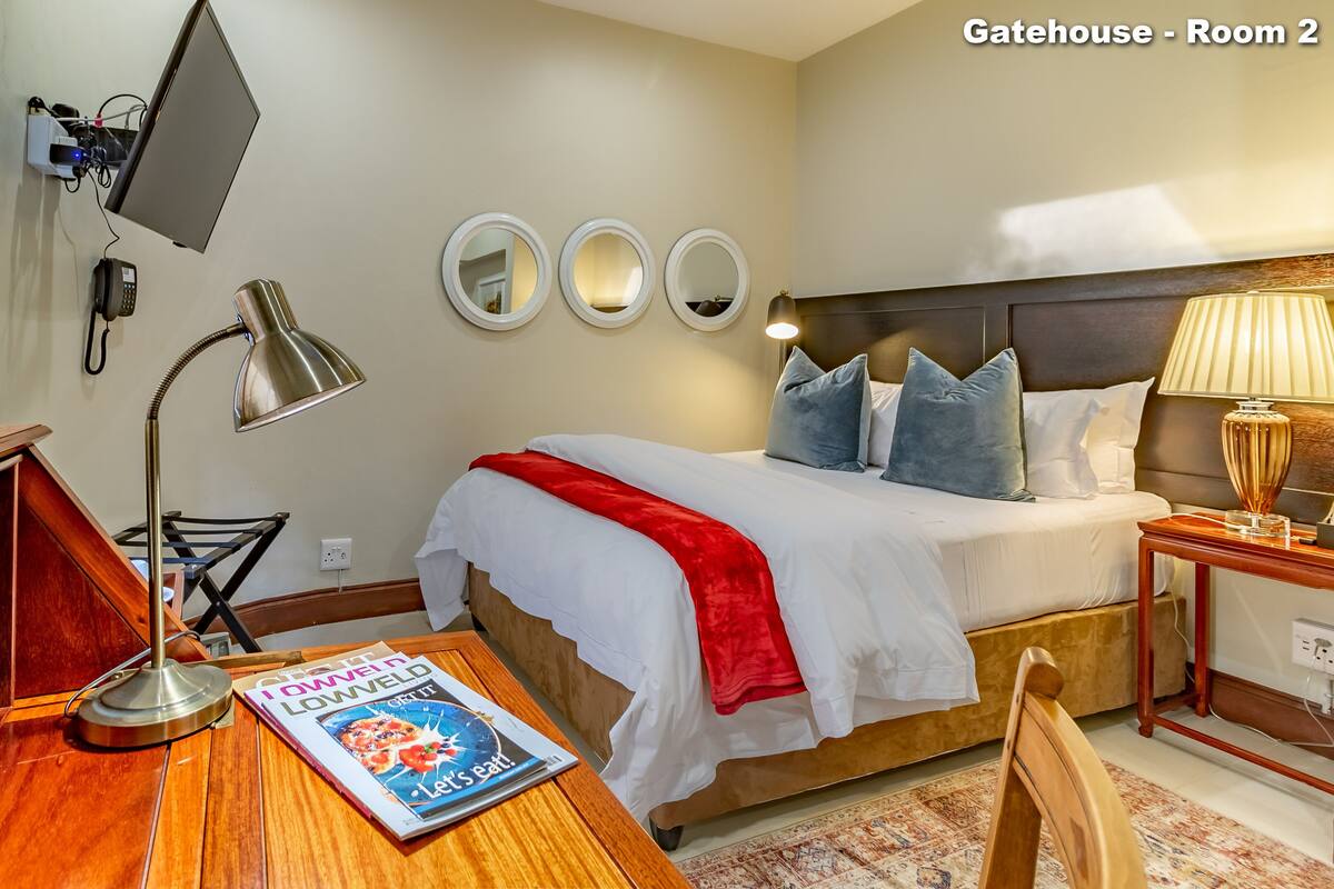 A hotel room with a bed, bedside lamp, desk with a laptop, and a magazine.