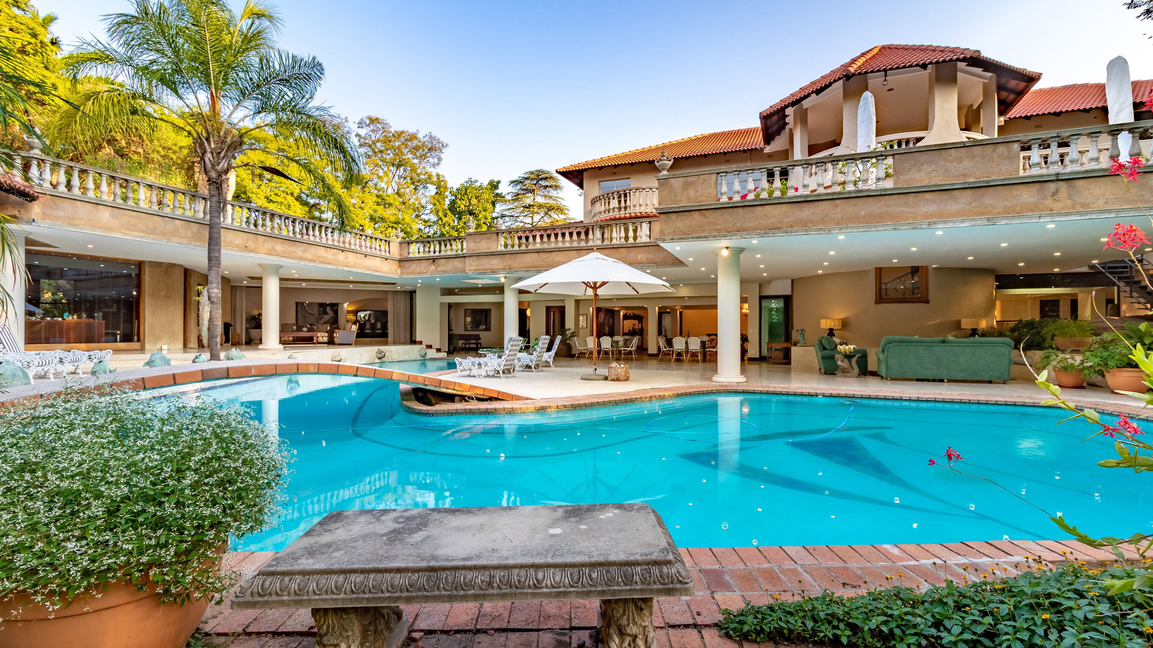 A large indoor swimming pool with a stone table in the foreground, surrounded by lounge chairs and a covered patio area.
