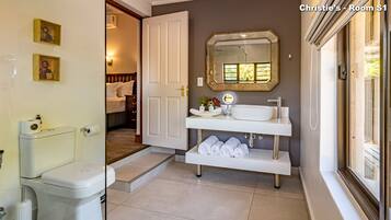 A modern bathroom with a toilet, sink, and mirror. There are towels and toiletries on the sink counter.