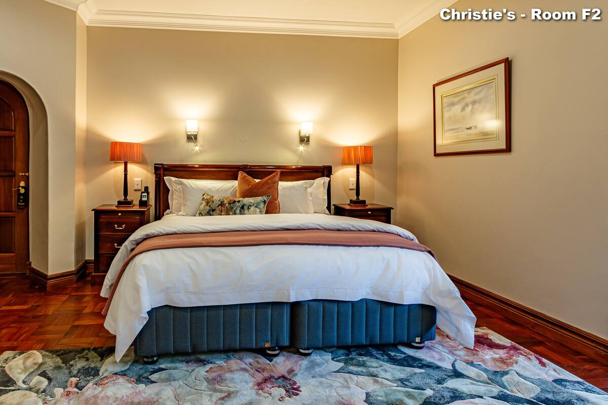A well-appointed bedroom with a large bed, two bedside tables, a nightstand, a wooden door, and a framed picture on the wall.