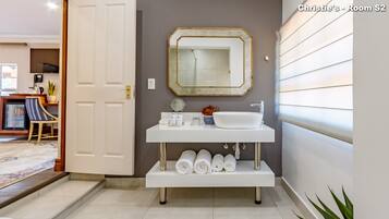 Une salle de bain moderne avec un meuble-lavabo blanc, un grand miroir et un évier. On y trouve des serviettes et des articles de toilette sur le meuble-lavabo.