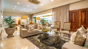 A spacious living room with a large sofa, a glass coffee table, and a patterned rug. There are two armchairs and a wooden cabinet in the background. - Christie's at 32 on Russell (Mbombela)