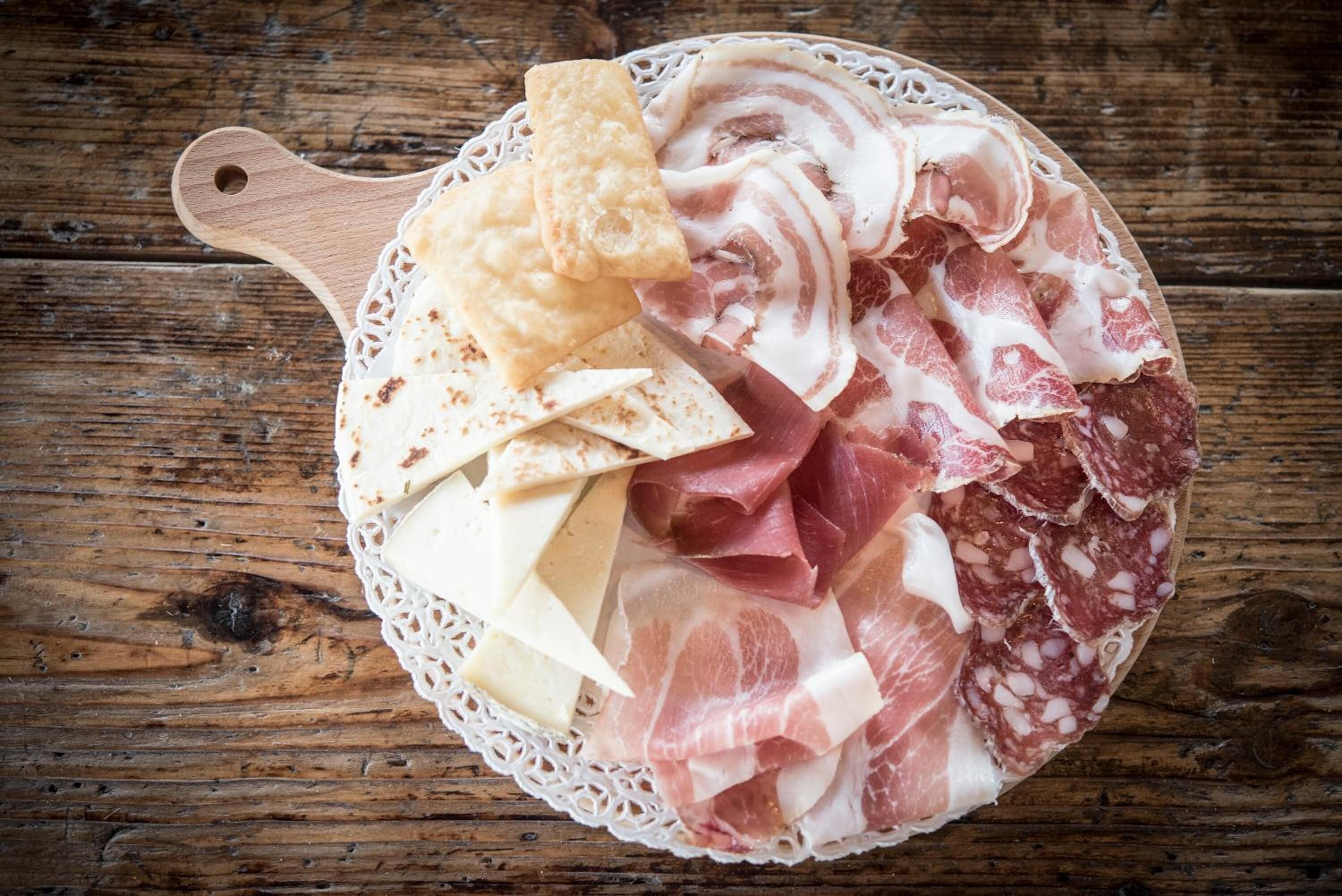 A wooden board with various cured meats and crackers on a rustic wooden table.