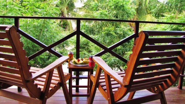 A wooden deck with two rocking chairs and a small table, surrounded by lush tropical foliage. - Residencial Bem Te Vi (Jijoca de Jericoacoara)
